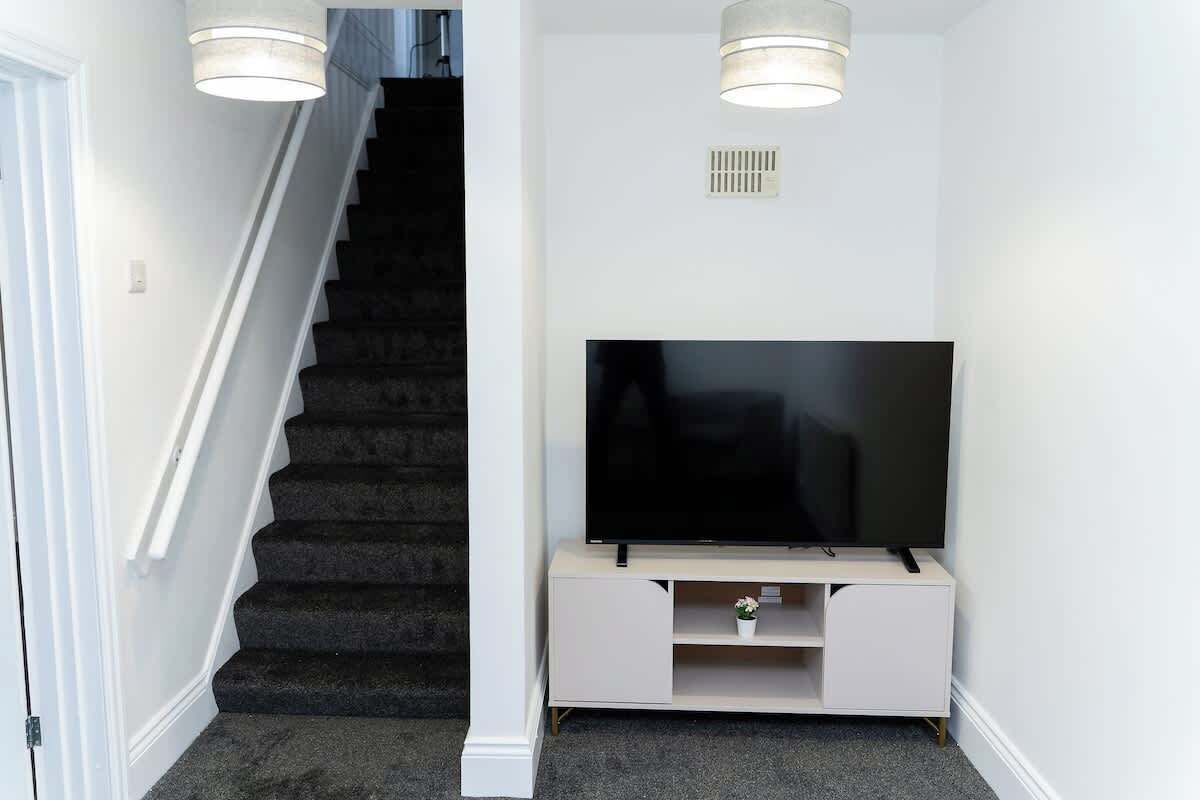 Eine Treppe mit Teppichstufen, ein Flachbildfernseher auf einem weißen Standfuß und zwei Pendelleuchten.