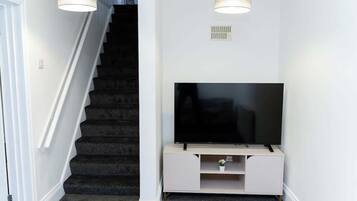 Eine Treppe mit Teppichstufen, ein Flachbildfernseher auf einem weißen Standfuß und zwei Pendelleuchten.