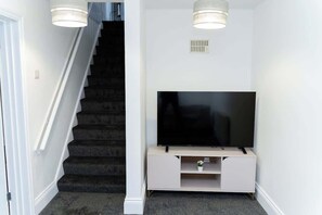 Eine Treppe mit Teppichstufen, ein Flachbildfernseher auf einem weißen Standfuß und zwei Pendelleuchten.