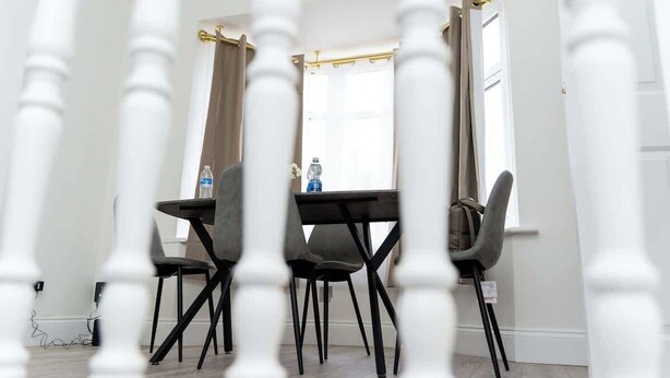 Een eethoek met een tafel en stoelen, een raam met gordijnen en een deur met gouden handvat.