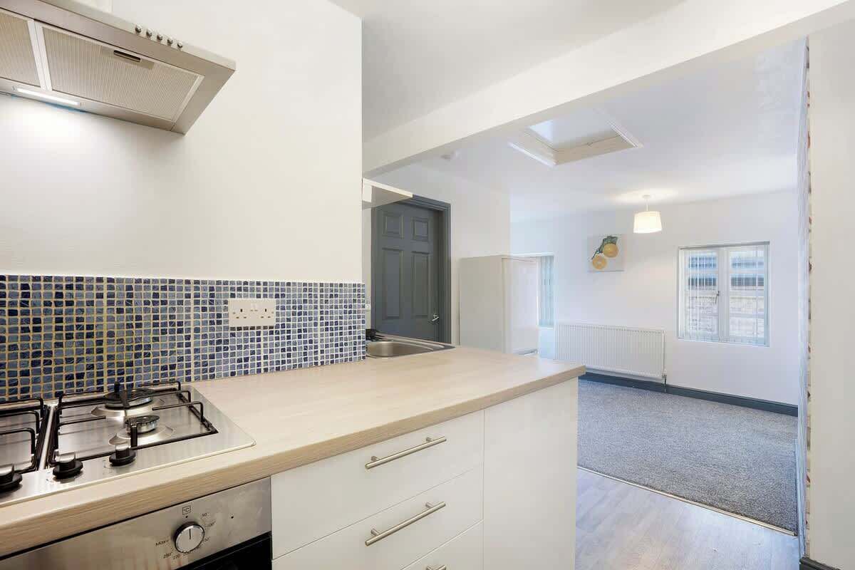 A kitchen with a gas stove, white cabinets, a tiled backsplash, and a view into the adjacent room.