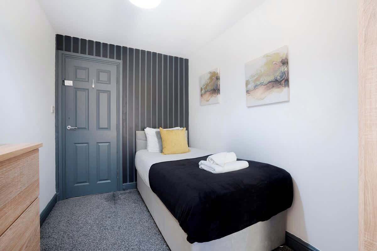 A bedroom with a bed, a door, a wall-mounted artwork, and a small wooden dresser.