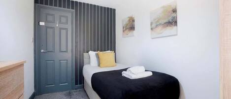 A bedroom with a bed, a door, a wall-mounted artwork, and a small wooden dresser.