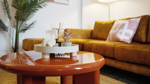 Ein modernes Wohnzimmer mit einem runden, orangefarbenen Tisch, einem gelben Sofa und einer Zimmerpflanze.