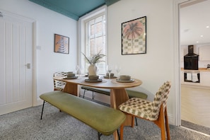 Un área de comedor con una mesa redonda, bancos, sillas y una planta en maceta.