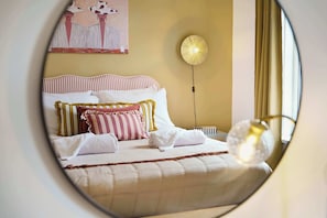 Una cama con ropa de cama a rayas, una lámpara de pared redonda y un cuadro en la pared.