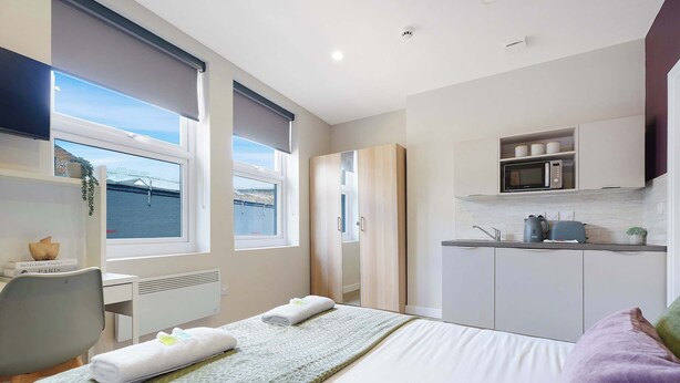 A modern hotel room with a bed, a desk, a kitchenette, and a view of the water. - Chic Middlesbrough Studio|Sleeps 2|By Stay with us (Middlesbrough)