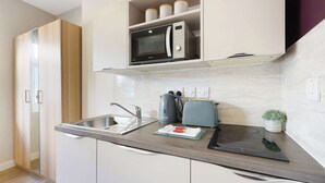 A modern kitchen with a microwave, kettle, toaster, and a small potted plant. - Chic Middlesbrough Studio|Sleeps 2|By Stay with us (Middlesbrough)