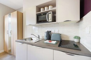 A modern kitchen with a microwave, kettle, toaster, and a small potted plant. - Chic Middlesbrough Studio|Sleeps 2|By Stay with us (Middlesbrough)