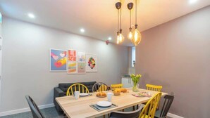 A dining area with a wooden table, yellow and black chairs, a sofa, and a kitchen in the background. - Chic Middlesbrough Studio|Sleeps 2|By Stay with us (Middlesbrough)