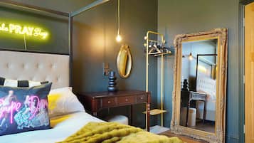 A bedroom with a bed, a bedside table, a mirror, and a neon sign.