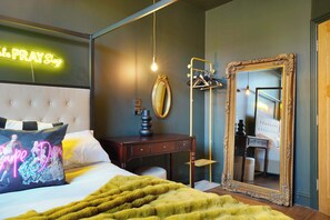 A bedroom with a bed, a bedside table, a mirror, and a neon sign.