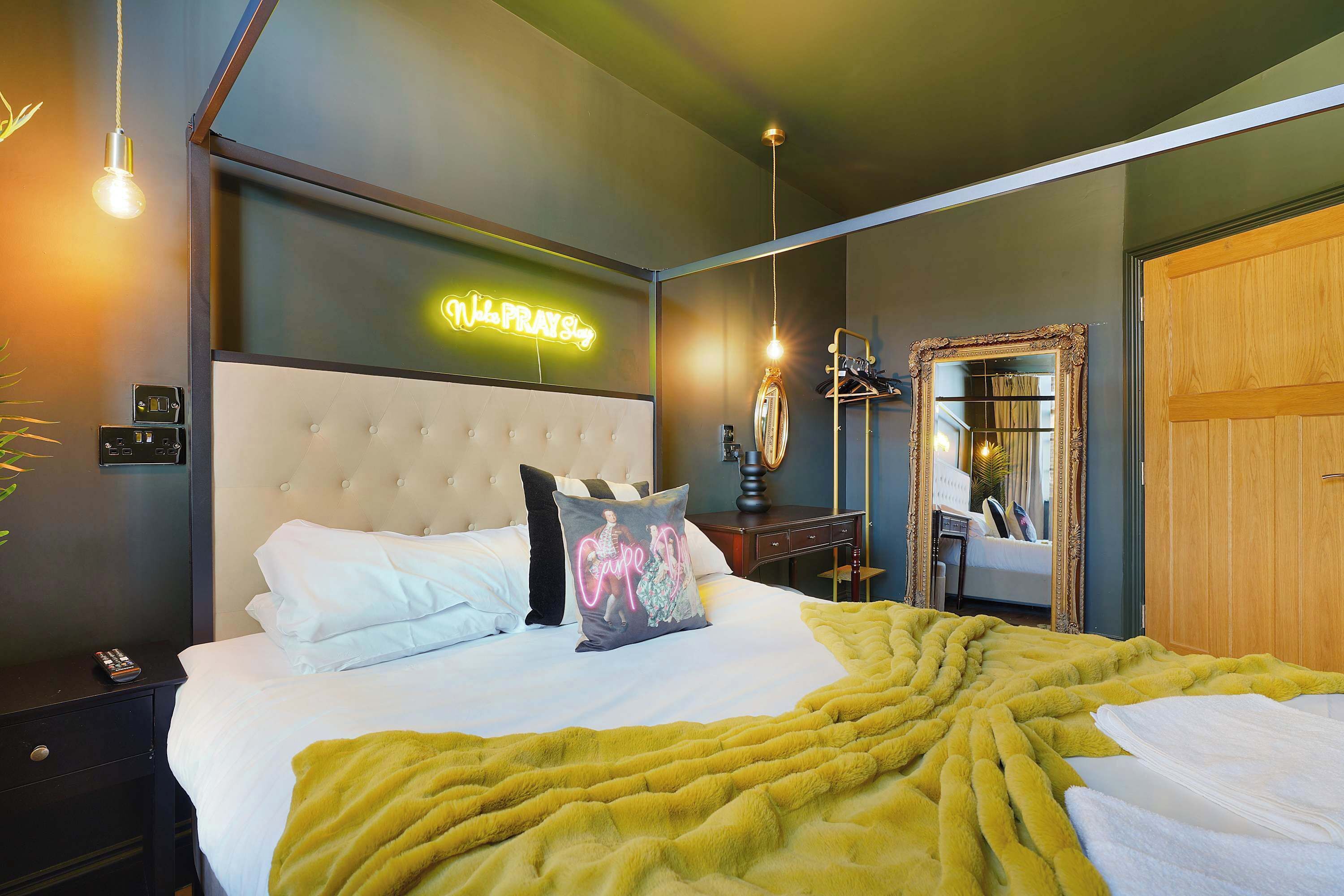 A modern bedroom with a tufted headboard, a neon sign, a mirror, and a yellow throw blanket.