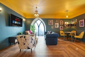 A modern living room with a fireplace, a television mounted on the wall, and a dining area with yellow chairs.
