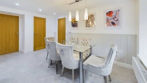 A dining area with a glass table and four chairs, wooden doors, and wall art. - Charming 3-Bedroom Home in the Heart of Stanhope (Stanhope)