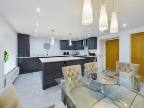 Une cuisine moderne avec des meubles de couleur sombre, un îlot central et des luminaires suspendus.