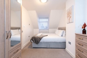 A bedroom with a bed, a dresser, a mirror, a window with blinds, and a ceiling light.