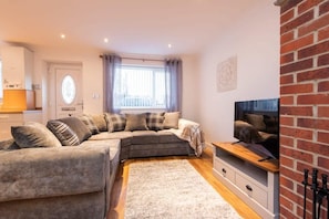 A living room with a sectional sofa, a flat-screen TV, a fireplace, and a window with curtains.