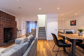 A modern living room with a fireplace, a sofa, a dining area with a table and chairs, and a staircase leading to another level.