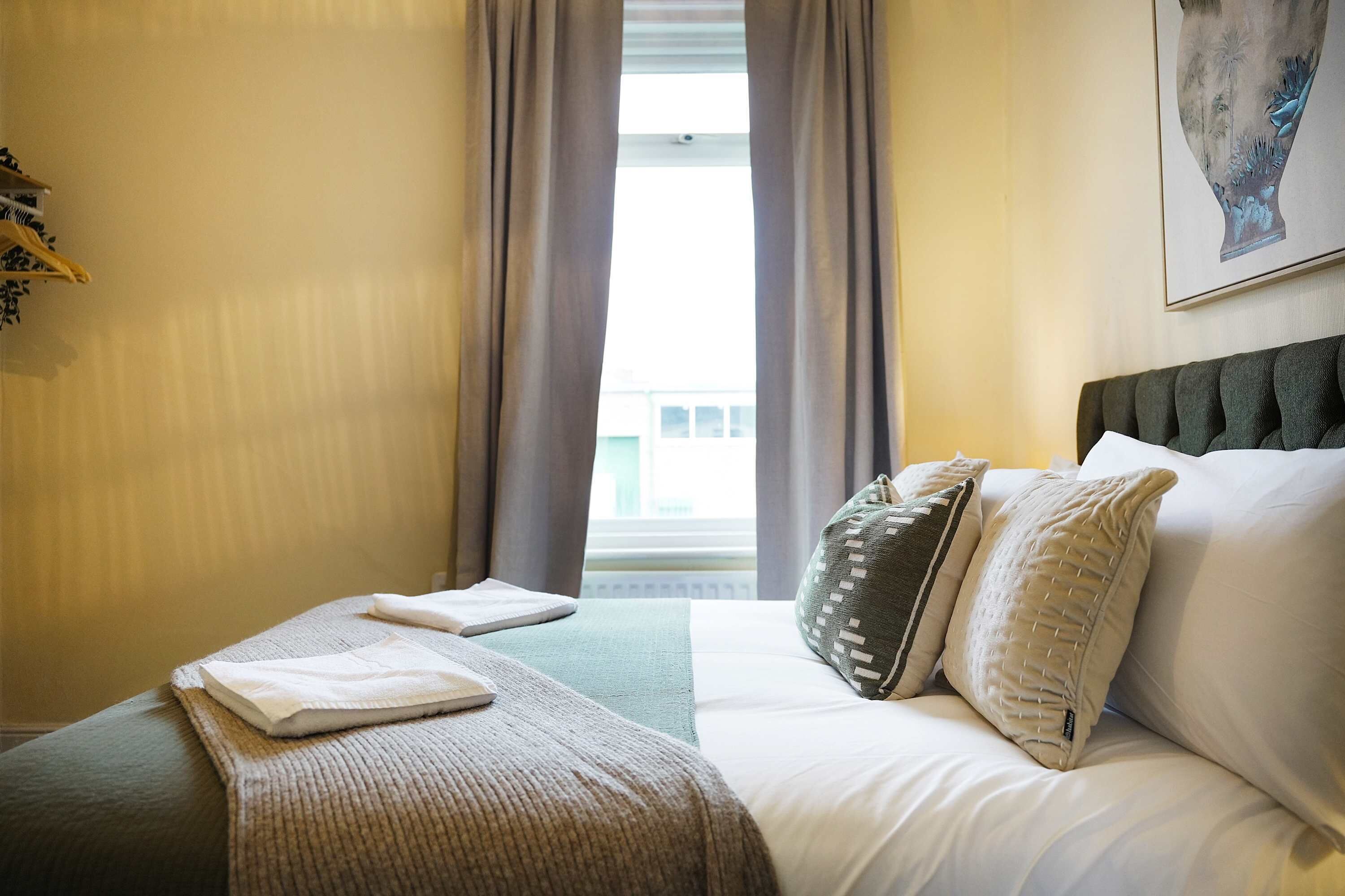 Hotelkamer met een bed, kussens, dekbed, raam met gordijnen en een aan de muur bevestigd kunstwerk.