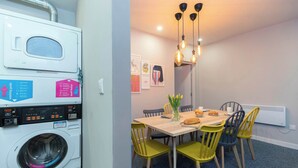 A compact living space with a washing machine, a dining area with a table and chairs, and a hanging light fixture. - Middlesborough City Centre Studio (Middlesbrough)