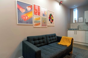 A living room with a dark grey sofa, a yellow throw blanket, and a wall with abstract art. - Middlesborough City Centre Studio (Middlesbrough)