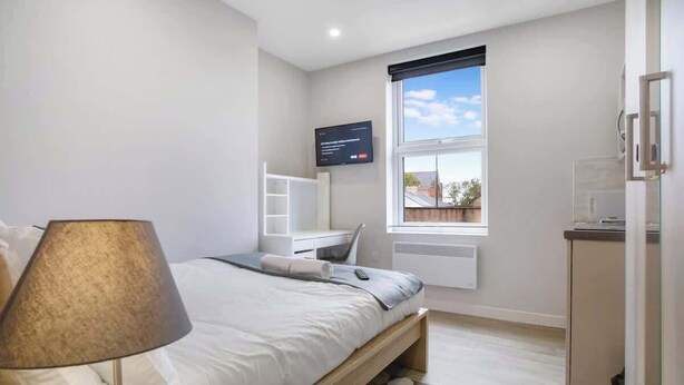 A bedroom with a bed, a TV mounted on the wall, a window with a view, and a desk with a chair. - Middlesborough City Centre Studio (Middlesbrough)