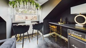 A modern kitchen with a black countertop, two black bar stools, a gold bar cart, and a Marshall amplifier. - Modern 4 Bed, Walk to Pubs, Shops and Countryside (Stanhope)