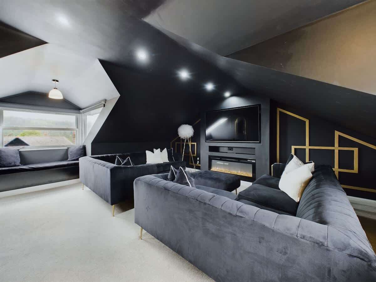 Ein modernes Wohnzimmer mit großem Flachbildfernseher, dunkelgrauen Sofas und einem Kamin.