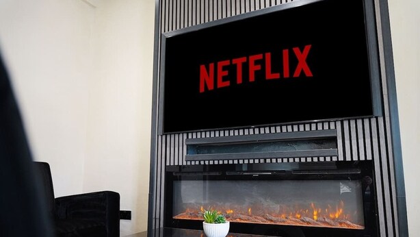 Una sala de estar moderna con chimenea, un televisor mostrando 'NETFLIX' y una planta pequeña sobre la repisa.