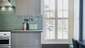 Una cocina con estufa, tostadora y ventana con persianas.
