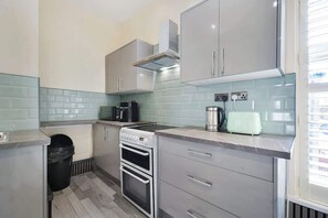 Eine kompakte Küche mit Gasherd, Backofen, Mikrowelle und Toaster. Es gibt Schränke und einen Mülleimer.