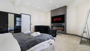 Un dormitorio moderno con cama, televisión montada en la pared y chimenea.