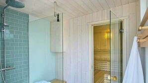 Casa de banho com teto de madeira, um banco, cabine de duche em vidro e um porta-toalhas.