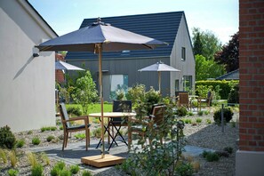 Eine Terrasse mit Gartenmöbeln, einem Tisch und zwei Sonnenschirmen.