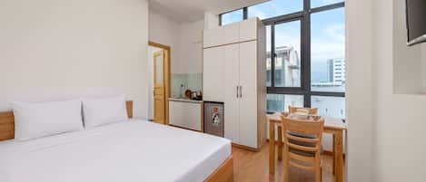Un dormitorio con cama, una kitchenette pequeña, una mesa de comedor con sillas y un ventanal grande.