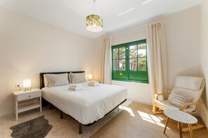 Ein Schlafzimmer mit Bett, Nachttisch, Sessel und einem Fenster mit Vorhängen.
