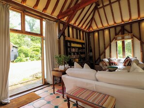 A cozy room with a sofa, a bookshelf, and a window with curtains. - Petworth Barn (Petworth)