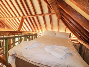 A bedroom with a wooden ceiling, a bed with white linens, and a nightstand with a lamp. - Petworth Barn (Petworth)