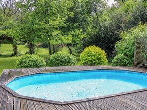 Piscina retangular com deck de madeira, cercada por vegetação exuberante e árvores.