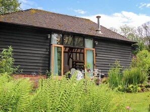A wooden house with a chimney, a glass door, and a garden with ferns and plants. - Petworth Barn (Petworth)