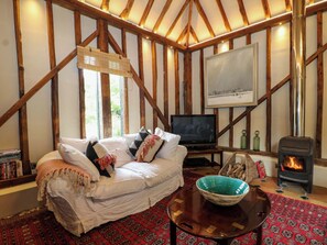 A cozy room with a wooden ceiling, a sofa, a television, a fireplace, and a patterned rug. - Petworth Barn (Petworth)