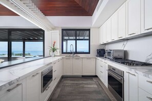 Eine moderne Küche mit weißen Schränken, einer Marmorarbeitsplatte, einem eingebauten Backofen und Meerblick.