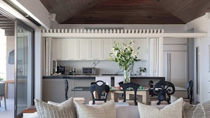 A modern living room with a glass coffee table, a sofa with patterned cushions, and a view of a kitchen in the background. - PH Azure: 4BR Oceanview Penthouse w/ Private Heated Infinity Pool & Rooftop (Punta Mita)