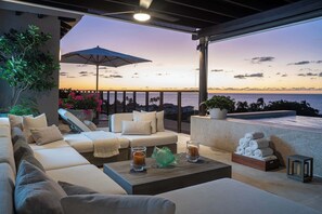 Ein moderner Außenbereich mit Meerblick bei Sonnenuntergang, mit einer Liege, einer Couch und einem Couchtisch mit Dekoration.