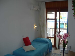 Ein Zimmer mit zwei Betten, einem Tisch mit Blumenvase und einem Balkon mit Blick.