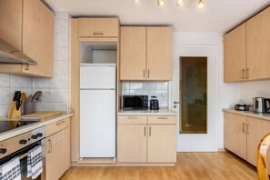 Una cocina compacta con armarios de madera, microondas, cafetera y refrigerador.