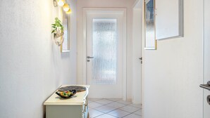 A hallway with a white door, a small table with a decorative item, and a wall-mounted light fixture.