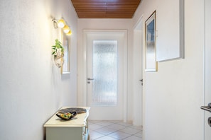 Un passadís amb una porta blanca, una taula petita amb un objecte decoratiu i un llum penjada a la paret.