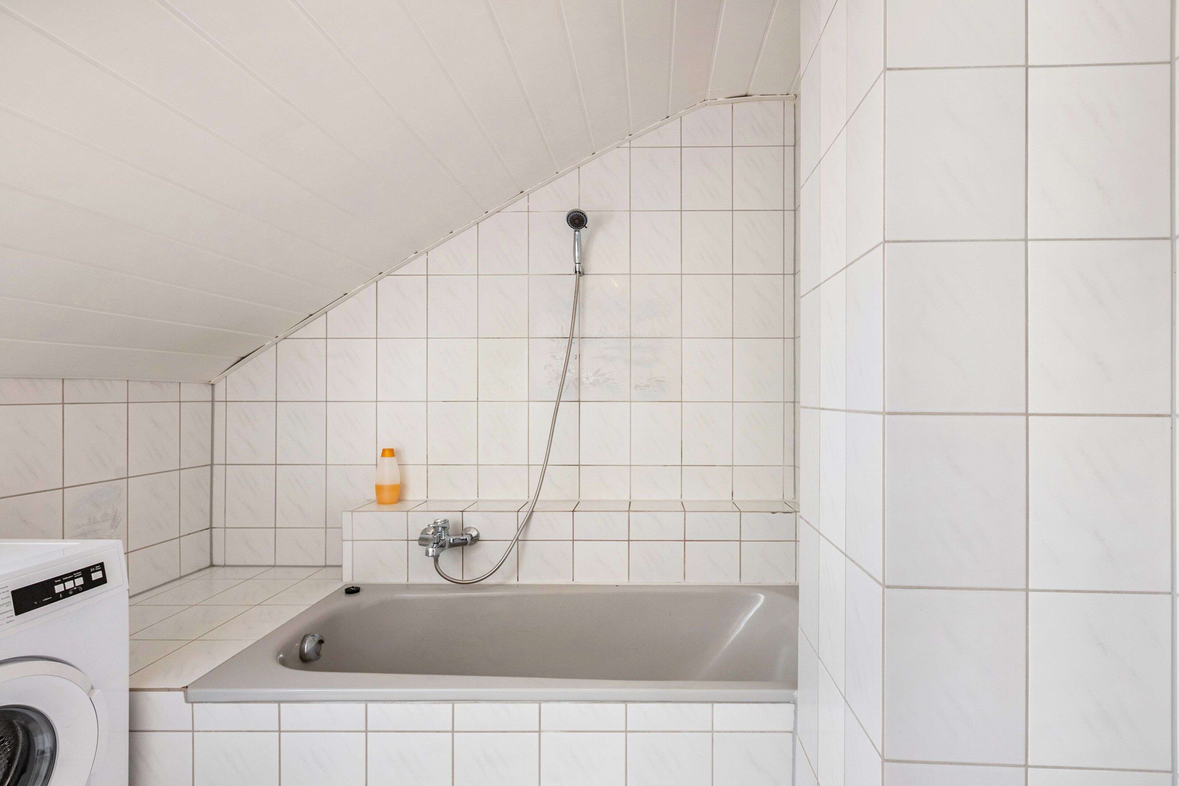 A bathroom with a bathtub, a washing machine, and a shower head.